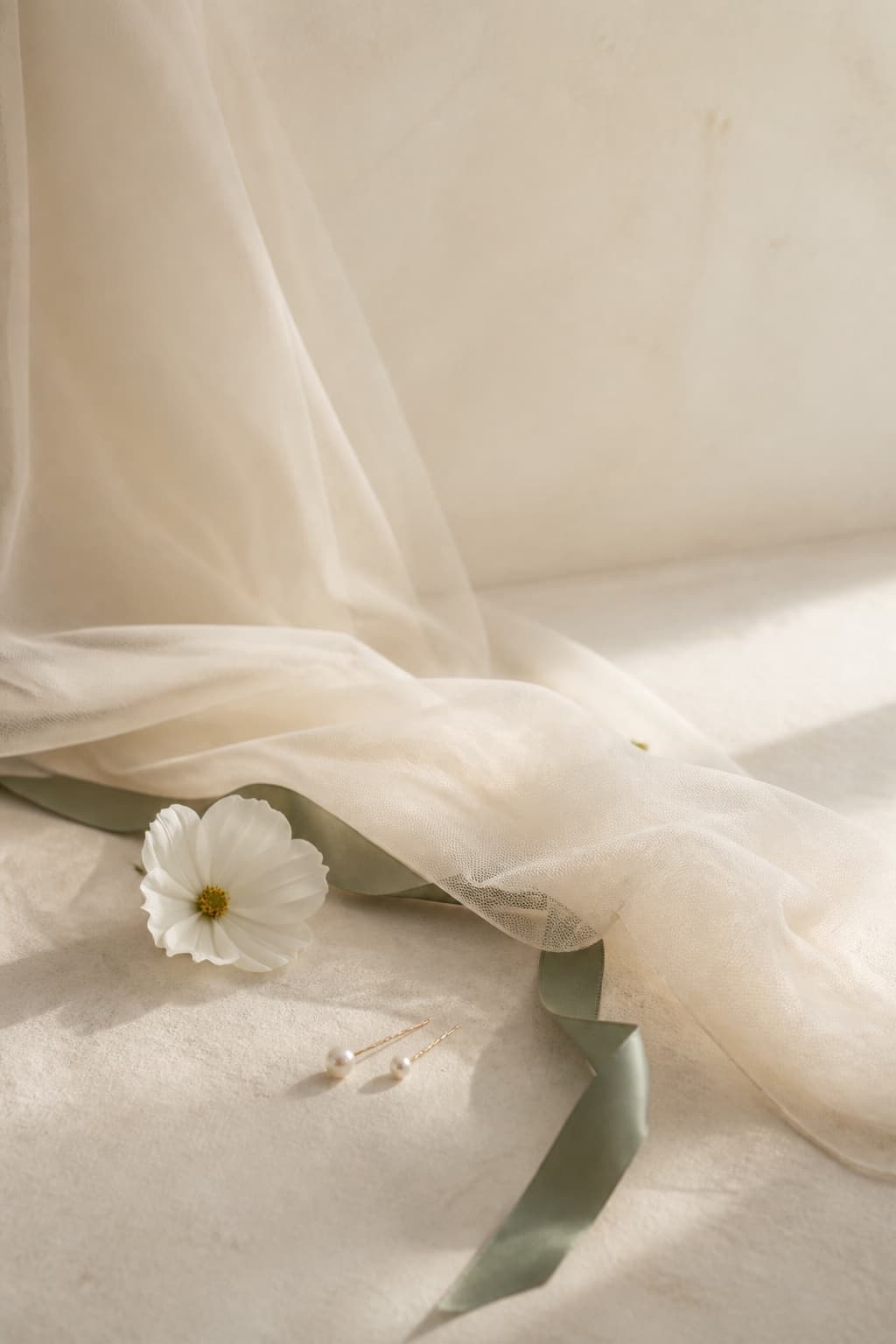 Conceptual bridal still life with ivory veil, white flower and sage ribbon